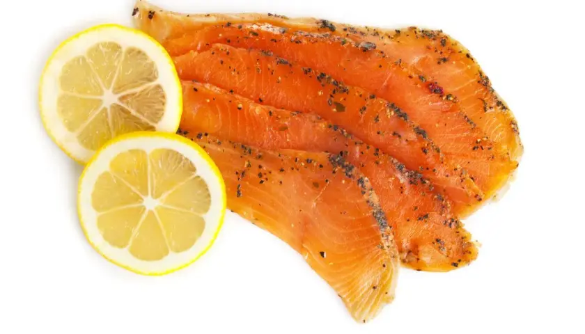 Skivor av gravad regnbåge med peppar och två citronskivor på vit bakgrund.