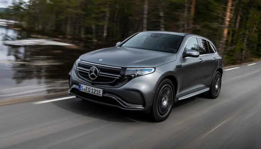 Szary Mercedes EQC jedzie po drodze wśród drzew.