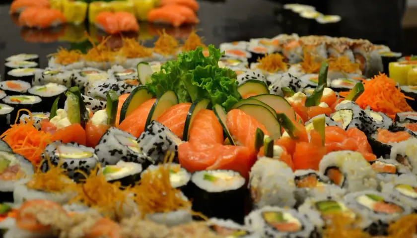 Mnóstwo sushi z łososiem, ogórkiem i sałatą. Wśród nich widać kawałki ryby maślanej, tworząc apetyczną kompozycję.
