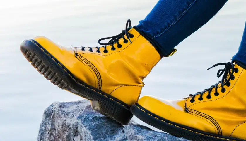 Botas amarillas de charol, con cordones negros, pisan una roca. Las botas de piel ceden ante la aventura.