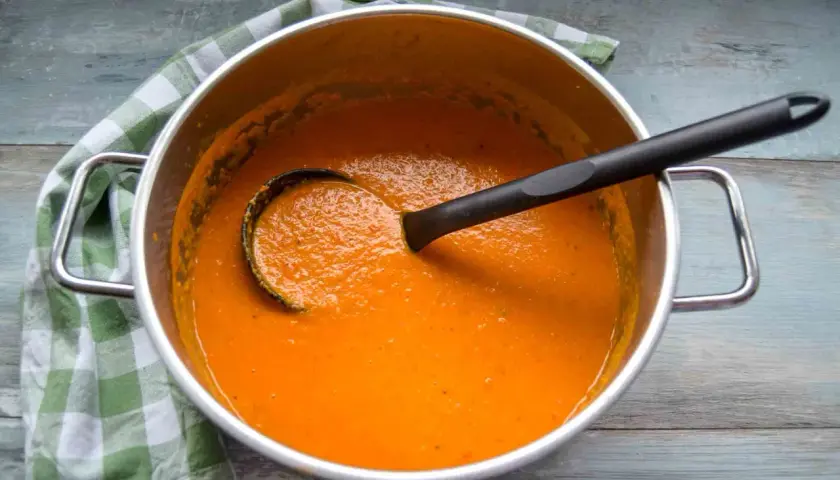 Ein Topf mit cremiger roter Linsensuppe mit Kokosmilch, bereit zum Servieren. Ein grünes Karotuch liegt daneben.