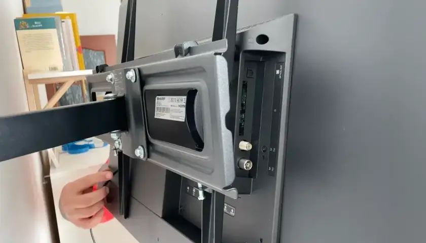 Montaż uchwytu do telewizora. Widoczne złącza i **urządzenia peryferyjne** podłączone do tyłu ekranu.