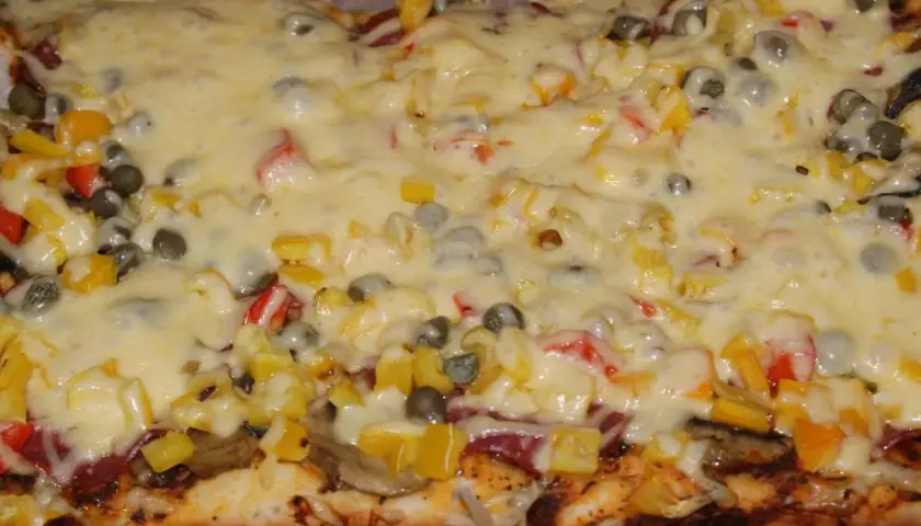 Pyszna pizza na grubym cieście z warzywami i roztopionym serem.