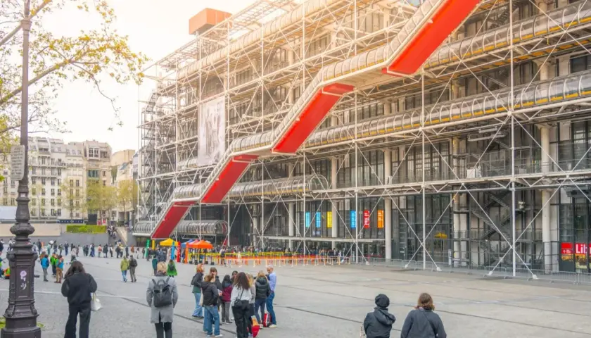 Widok na Centre Pompidou z czerwonymi schodami ruchomymi i ludźmi spacerującymi po placu.