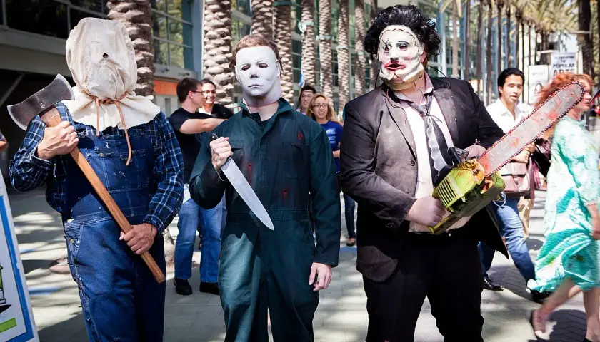 Trzech mężczyzn w strojach znanych postaci z horrorów: jeden z workiem na głowie i siekierą, drugi jako Michael Myers z nożem, trzeci jako Leatherface z piłą łańcuchową. Groźny slasher na konwencie.