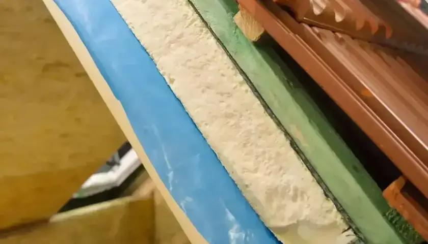 Warstwa izolacyjna z materiału pu w przekroju dachu, widoczna pianka, folia niebieska i dachówka.