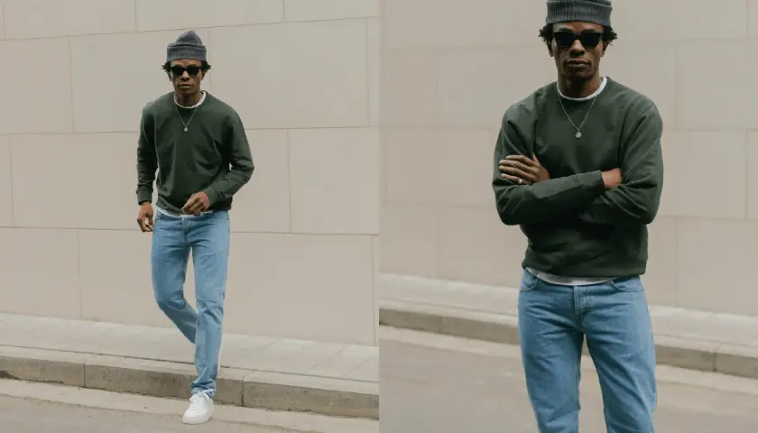 Un homme porte une tenue jean bleu décontractée, un pull vert foncé et un bonnet gris.