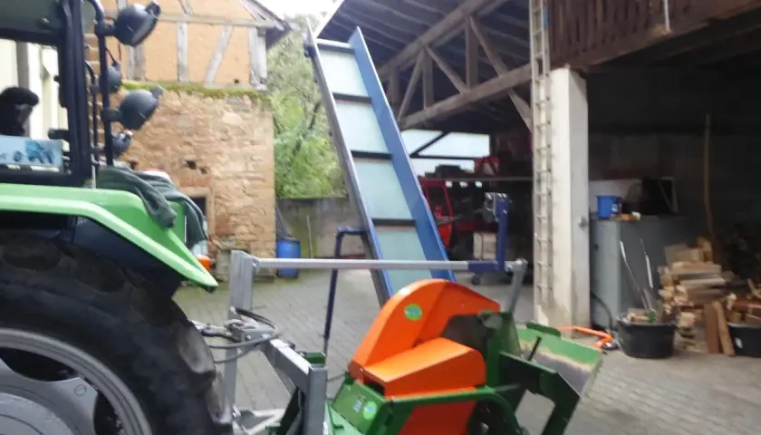 Gebrauchte Kreissäge mit Förderband, bereit für den Holzeinschlag. Ein Traktor steht daneben.