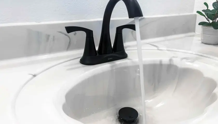 Rubinetto nero moderno in un lavandino bianco, con acqua che scorre. Uno stilema fad che aggiunge un tocco di eleganza.
