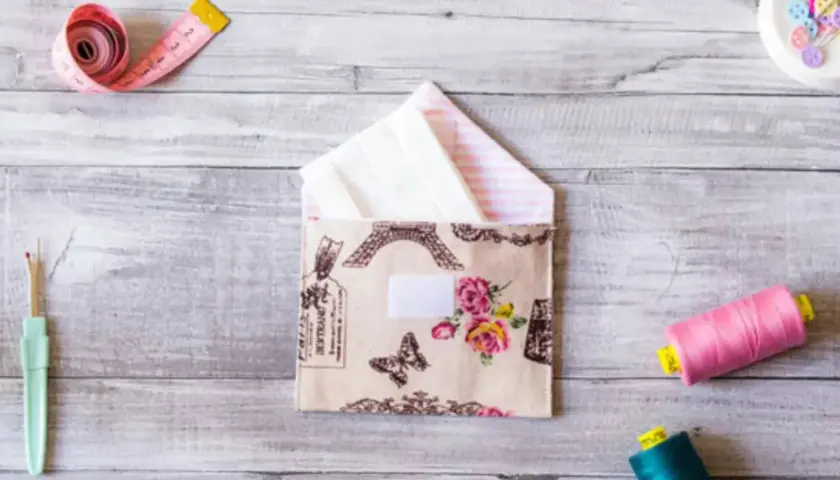 Sobres de tela con diseño de París y flores, junto a carretes de hilo, cinta métrica y descosedor.