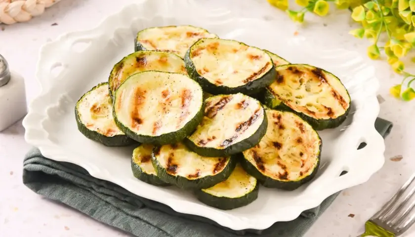 Rodajas de calabacín a la plancha, con marcas de parrilla doradas, servidas en un plato blanco festoneado.