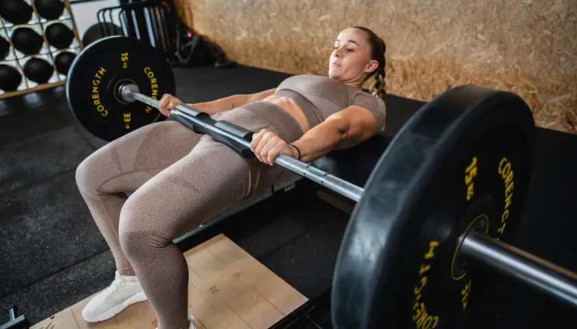 Kobieta wykonuje FBW Sakera, ćwiczenie na pośladki z ciężarem na biodrach.