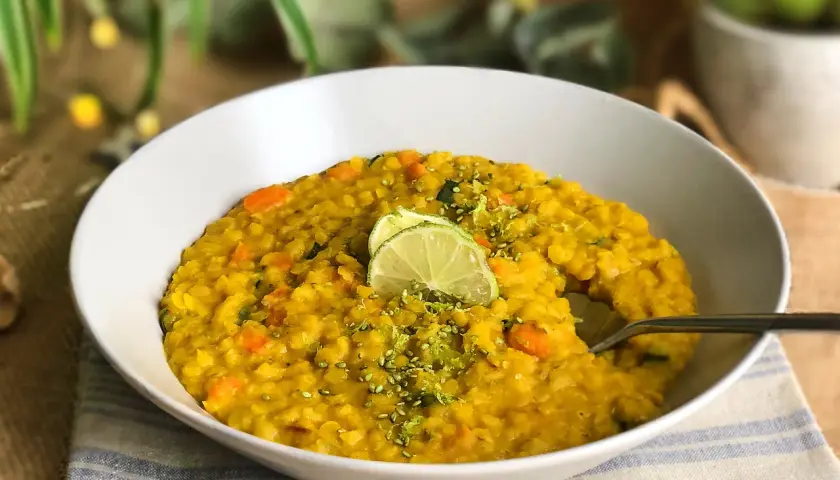 Un tazón de lentejas al curry con zanahoria y calabacín, decorado con rodajas de lima y ralladura.