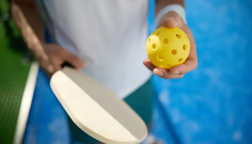 Gracz trzyma rakietkę i żółtą piłeczkę. Idealny sprzęt do treningu mobility i gry w pickleball.