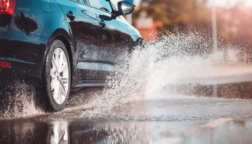 Coche negro salpicando agua. Para evitar el aquaplaning, reduce la velocidad y mantén tus neumáticos en buen estado.