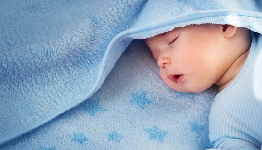 Sover gott under ett mjukt, blått täcke med stjärnor. Liten bebis svettas lite i sömnen.