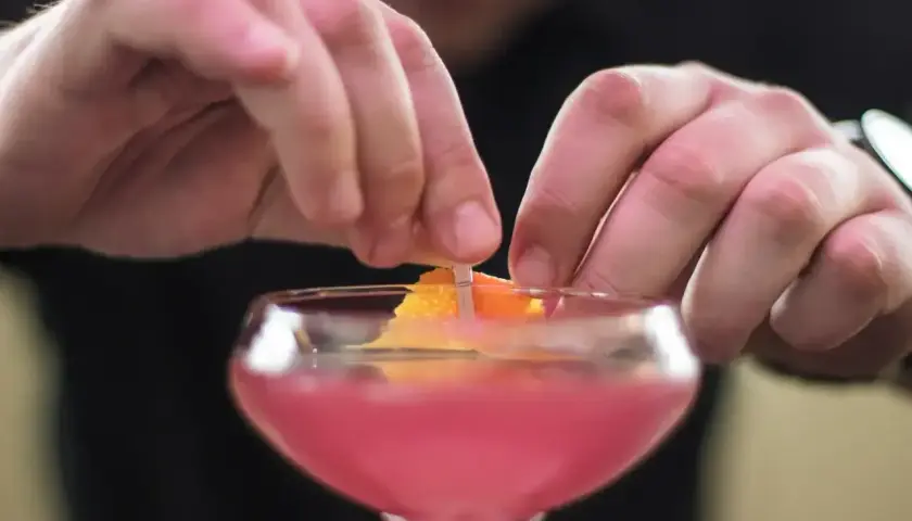 Dłonie barmana ozdabiają drinka skórką pomarańczy. To klasyczny cosmopolitan, gotowy na wieczór w wielkim mieście.