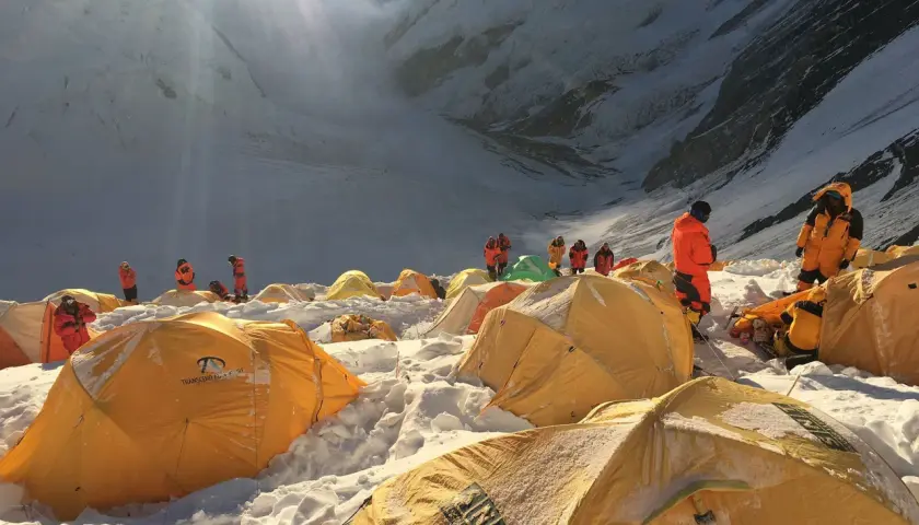 Bergsteiger in orangefarbenen Anzügen bereiten sich auf den Aufstieg vom Mount Everest Camp 4 vor. Gelbe Zelte sind im Schnee verstreut.