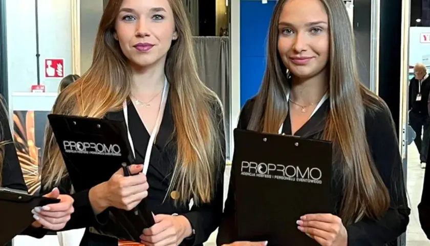 Dwie uśmiechnięte hostessa z agencji PROPROMO trzymają teczki z logo firmy.