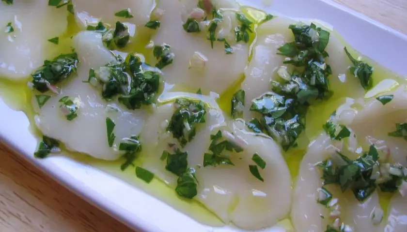 Délicieux carpaccio de saint jacques crues, nappé d'une vinaigrette aux herbes fraîches et à l'ail. Un plat léger et savoureux.