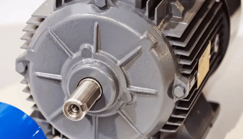 Dettaglio di un motore elettrico grigio, con albero motore visibile e una targhetta dorata.