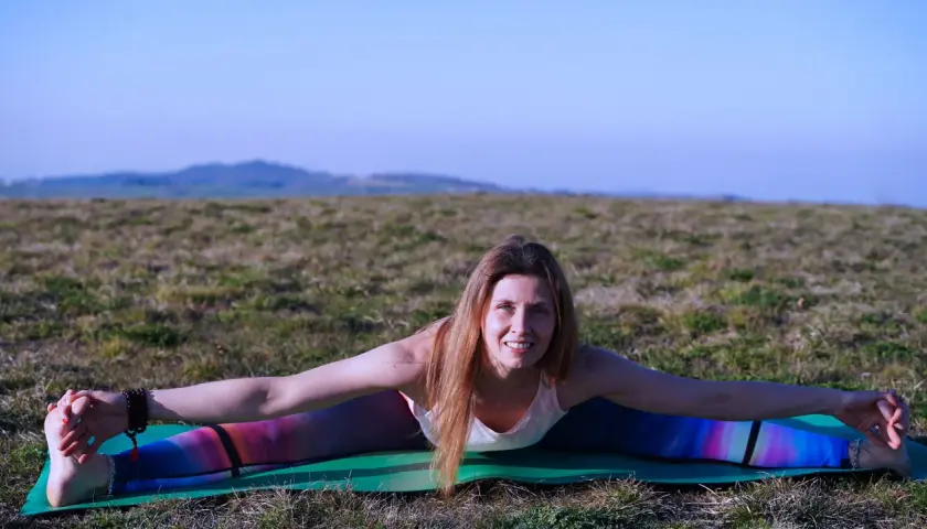 Donna in posa yoga all'aperto, con le gambe divaricate, che lavora sul primo chakra sessualità.