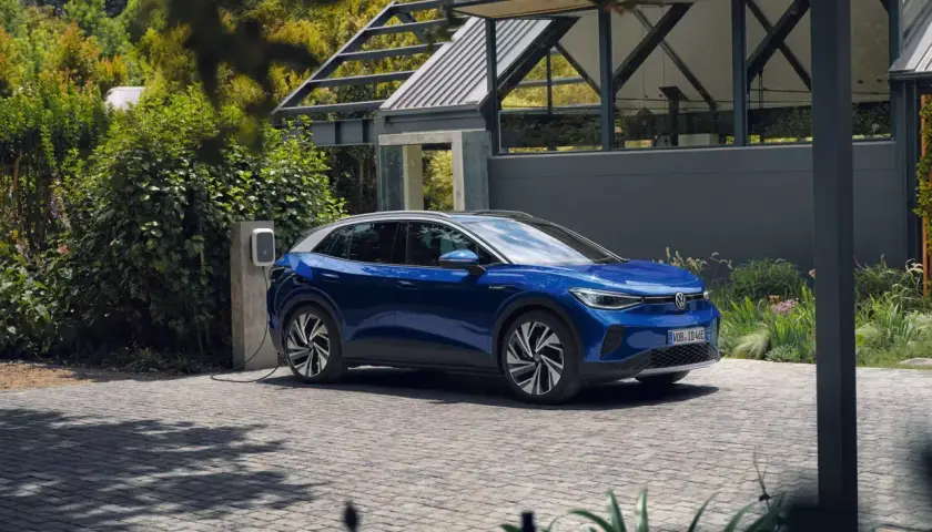 Niebieski VW ID.4 ładuje się przy nowoczesnym domu. Elektryczny SUV stoi na podjeździe, podłączony do ładowarki.