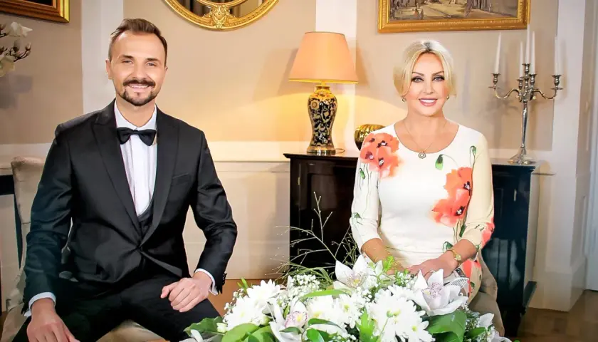 Mężczyzna w garniturze i kobieta w sukience w kwiaty siedzą obok siebie.
