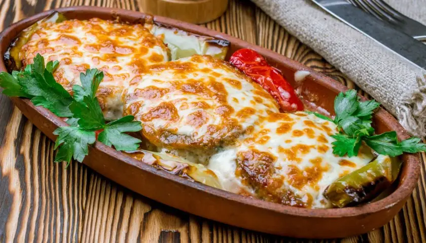 Kotlet po góralsku zapieczony z serem i warzywami w glinianym naczyniu, udekorowany natką pietruszki.