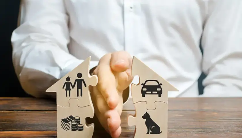 Dwa domy z puzzli rozdzielone ręką. Jeden symbolizuje rodzinę i pieniądze, drugi auto i psa. Ilustracja sytuacji, kiedy ustaje wspólność majątkowa.