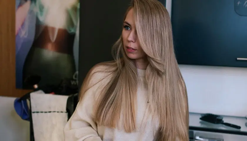 Dziewczyna z długimi, mysi blond włosami, ubrana w beżowy sweter.