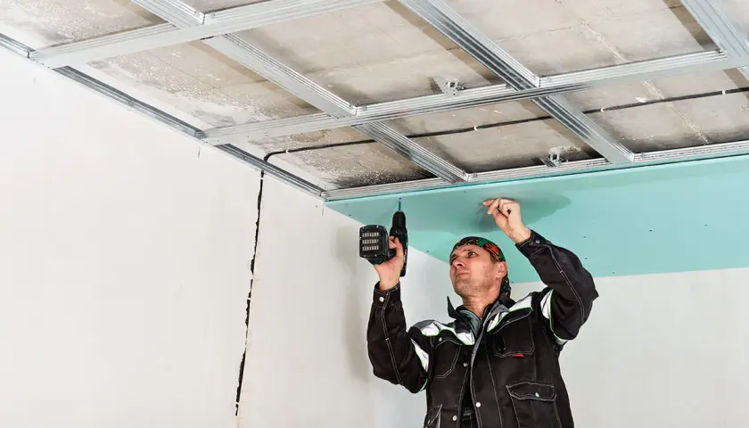 Un ouvrier installe une plaque de plâtre sur une structure métallique, créant ainsi un plafond technique.