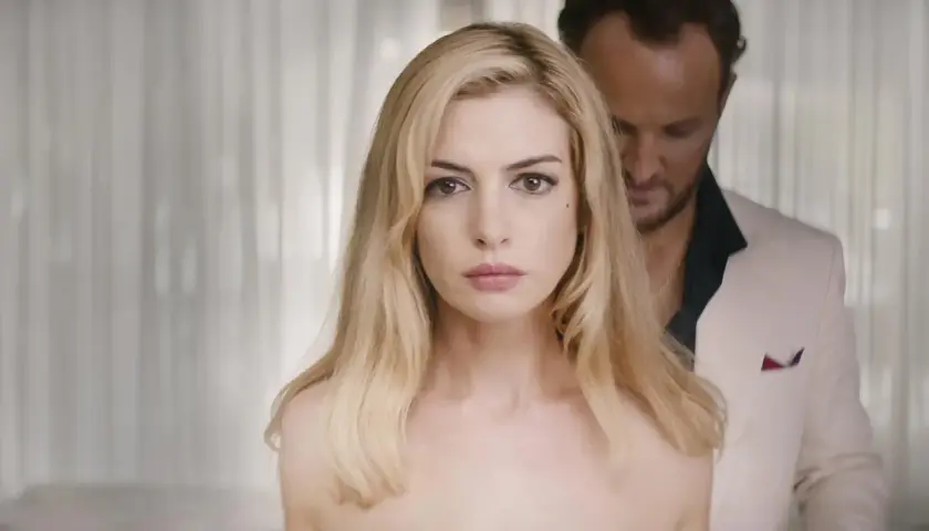 Anne Hathaway, protagonista de "L'isola dell'inganno", con uno sguardo intenso. Dietro di lei, un uomo in giacca bianca.