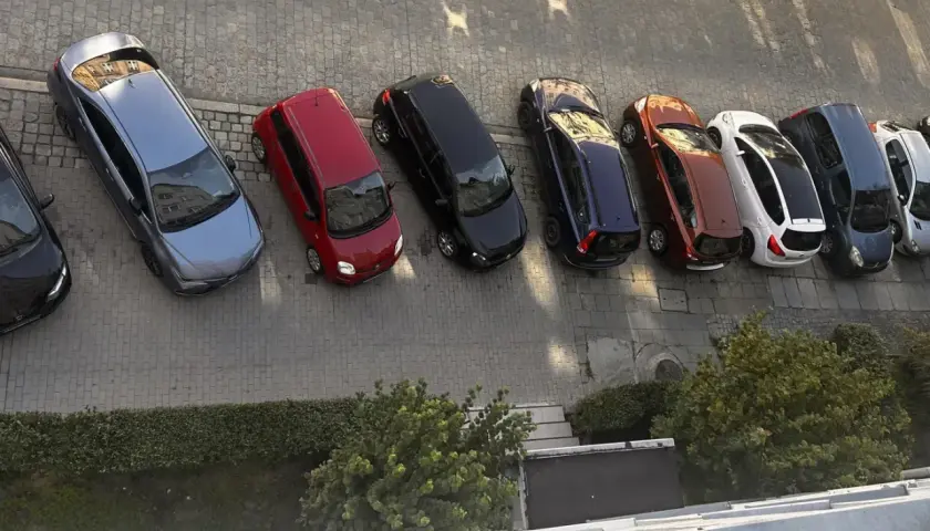 Szary samochód, czerwony, czarny, granatowy, rudy, biały, ciemnogranatowy i srebrny stoją na parkingu. Może to być inspiracja do wypełnienia wniosku o miejsce parkingowe wzór.