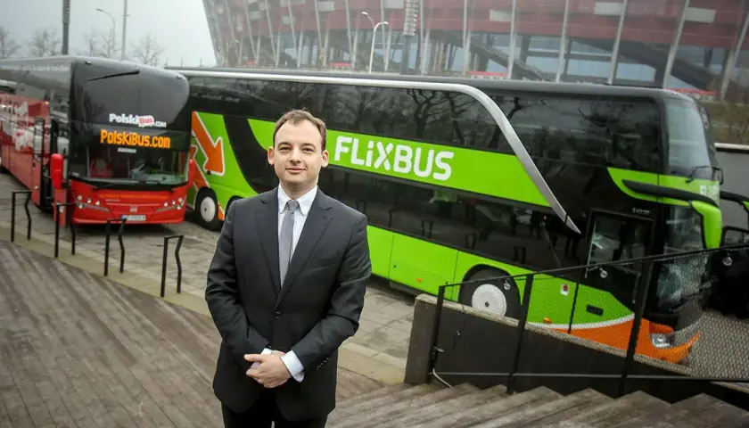 Mężczyzna w garniturze stoi przed zielonym autokarem Flixbus i czerwonym autokarem Polskibus.