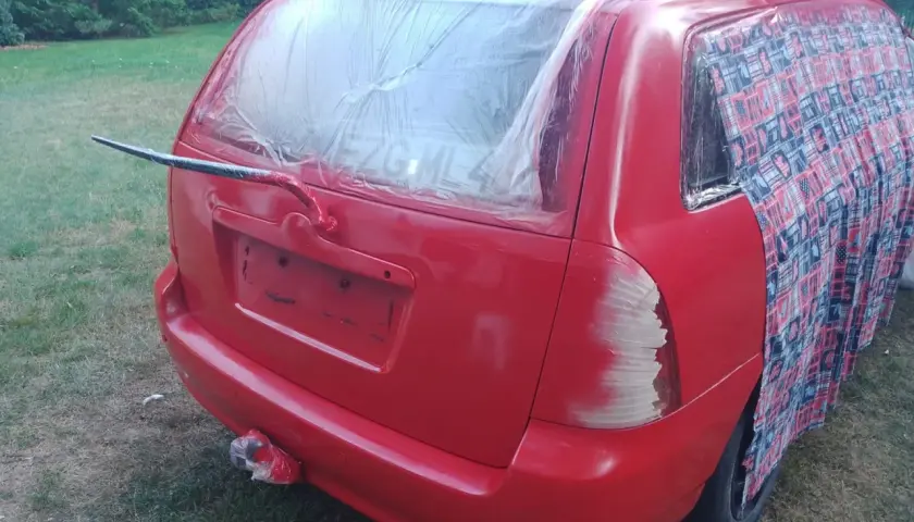 Czerwony samochód z zakrytą folią tylną szybą i częścią karoserii, przygotowywany do malowania.