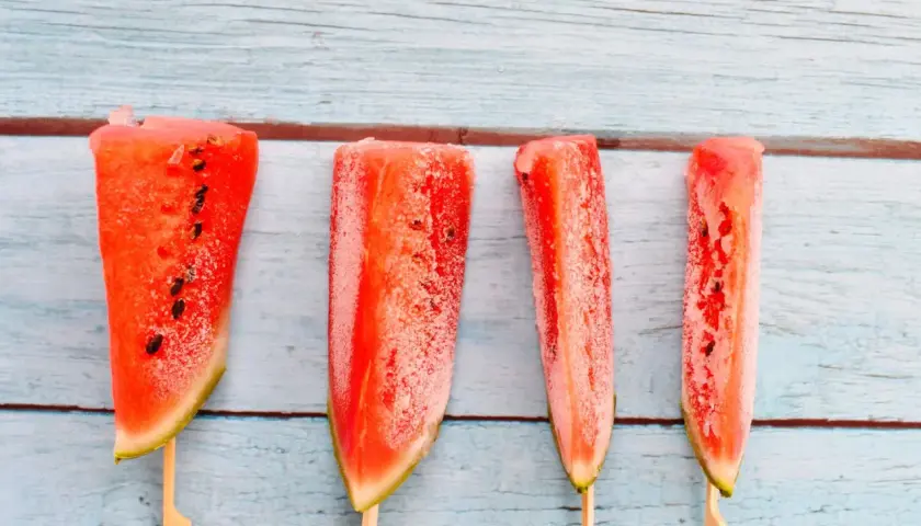 Vier Wassermelonenstücke auf Stäbchen, bereit zum Wassermelone einfrieren. Perfekt für heiße Sommertage.