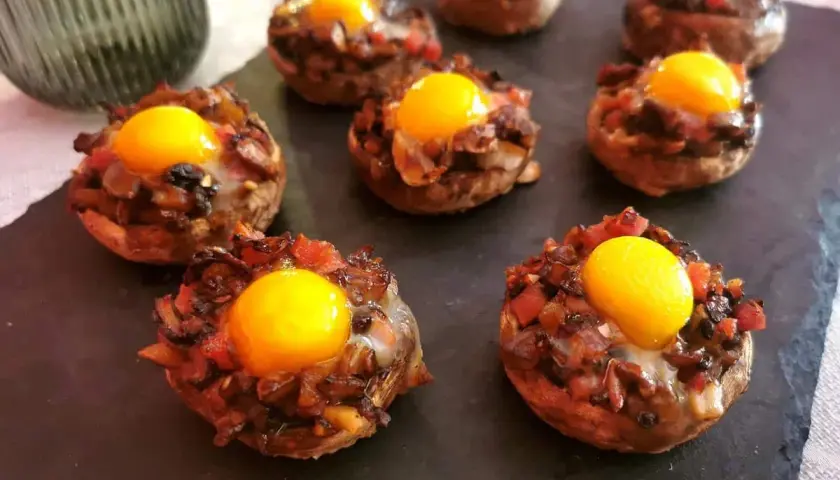 Champiñones rellenos con huevo y trocitos de tomate y cebolla, listos para disfrutar.