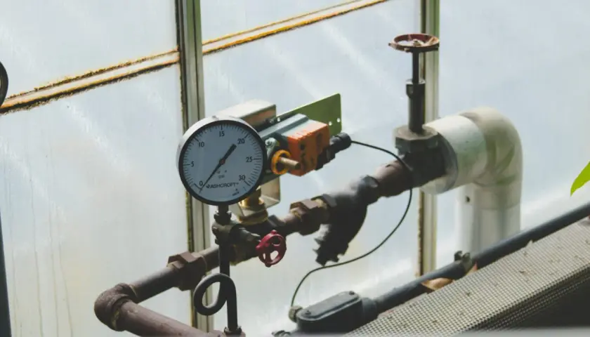 Manometr wskazuje prawidłowe ciśnienie w instalacji co. Rury i zawory są widoczne.