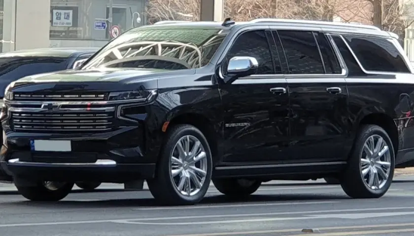 Czarny Chevrolet Suburban, który wygląda jak największe auto na świecie, z chromowanymi felgami i błyszczącą atrapą chłodnicy.