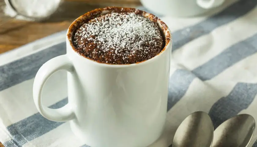 Un delizioso mug cake al cioccolato, spolverato di zucchero a velo, pronto per essere gustato.