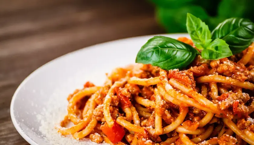 Talerz spaghetti z ragù mięsnym, posypany parmezanem i udekorowany listkami bazylii.