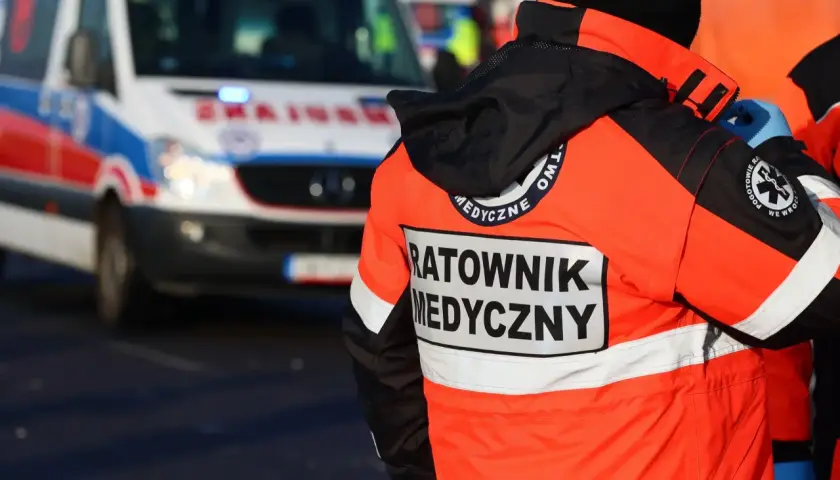Ratownik medyczny w pomarańczowej kurtce stoi obok karetki.