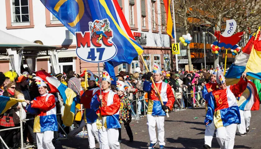 Bunte Kostüme und Fahnen beim Fasching 2026. Menschen feiern ausgelassen in der Stadt.