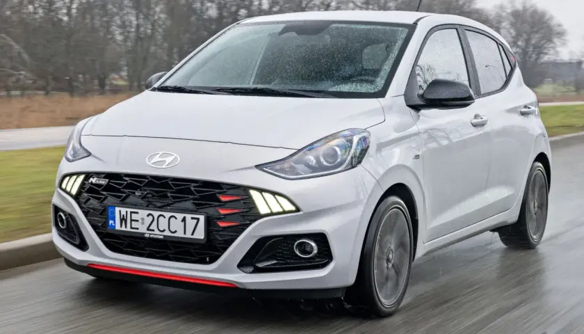 Biały Hyundai i10 N Line w ruchu, z widocznym grillem i światłami. Sprawdź aktualną hyundai i10 cena.