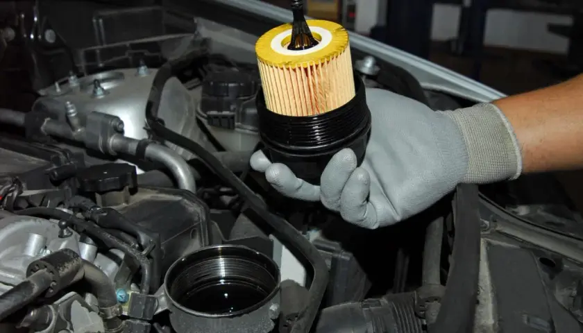 Mano guantata mostra il filtro olio motore appena estratto dal suo alloggiamento, pronto per la sostituzione.