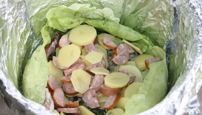 Gotowe dania na ognisko: ziemniaki, kiełbasa i kapusta zawinięte w folię aluminiową, czekają na pieczenie.