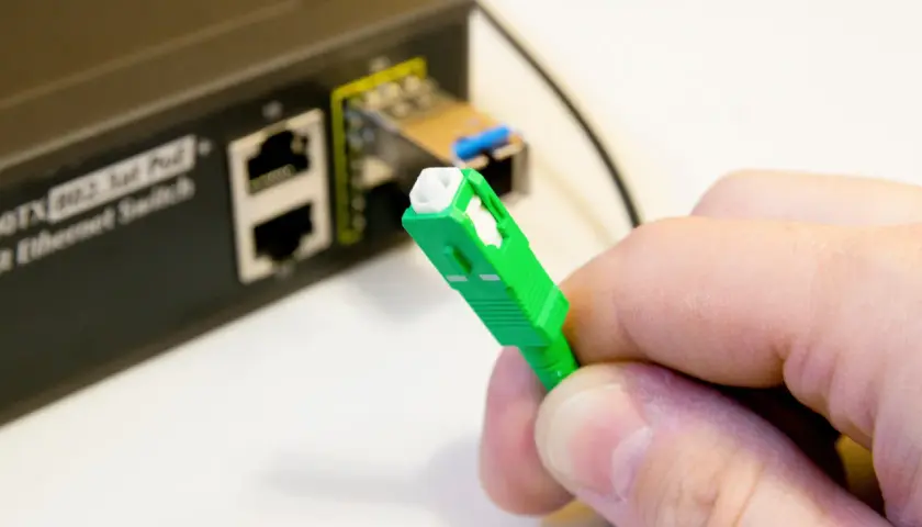 Zielona wtyczka światłowodu gotowa do podłączenia do switcha w bloku. Szybki internet w zasięgu ręki.
