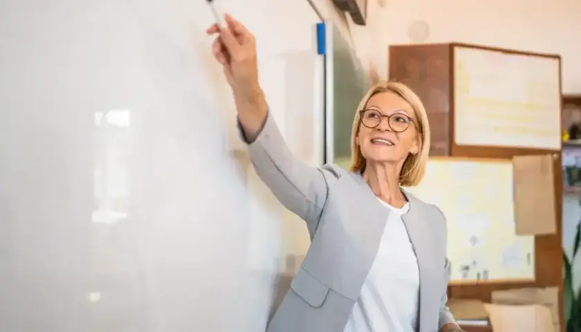 Nauczycielka z markerem przy tablicy, omawiająca rozporządzenie dotyczące oceny pracy nauczyciela.