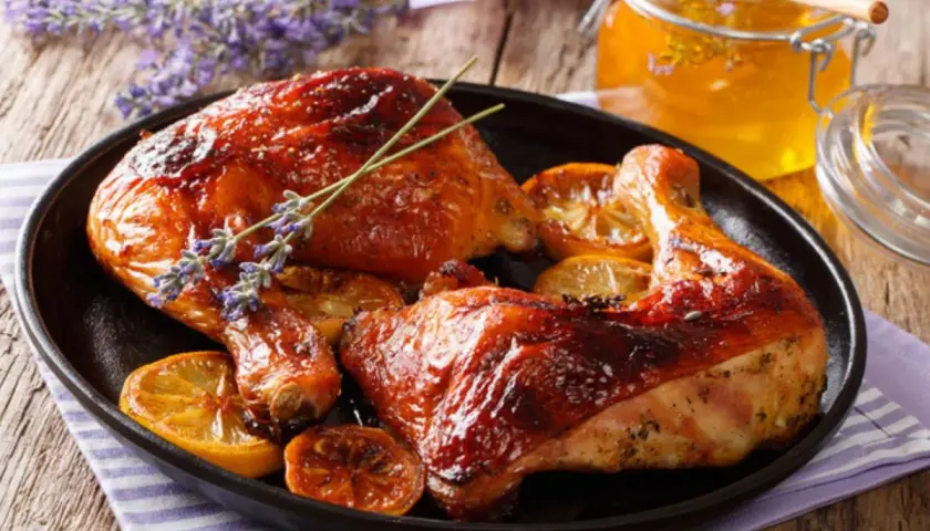 Muslos de pollo al horno dorados y jugosos, servidos con rodajas de limón y un toque de lavanda. Un tarro de miel dorada acompaña este delicioso plato.